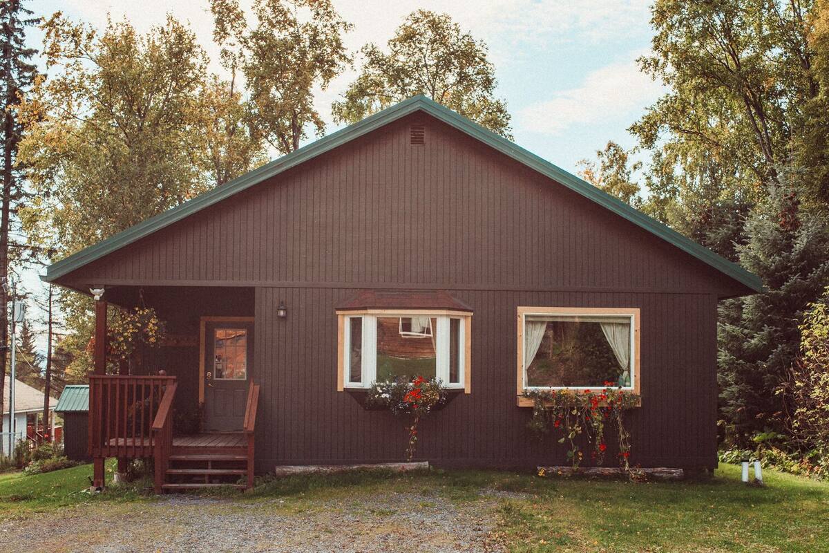 A wooden cabin with a porch, two windows, and flower boxes.