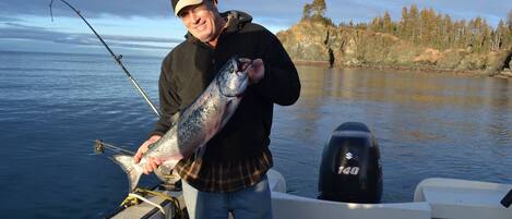 A person holding a fish on a boat with a rocky shoreline and trees in the background.