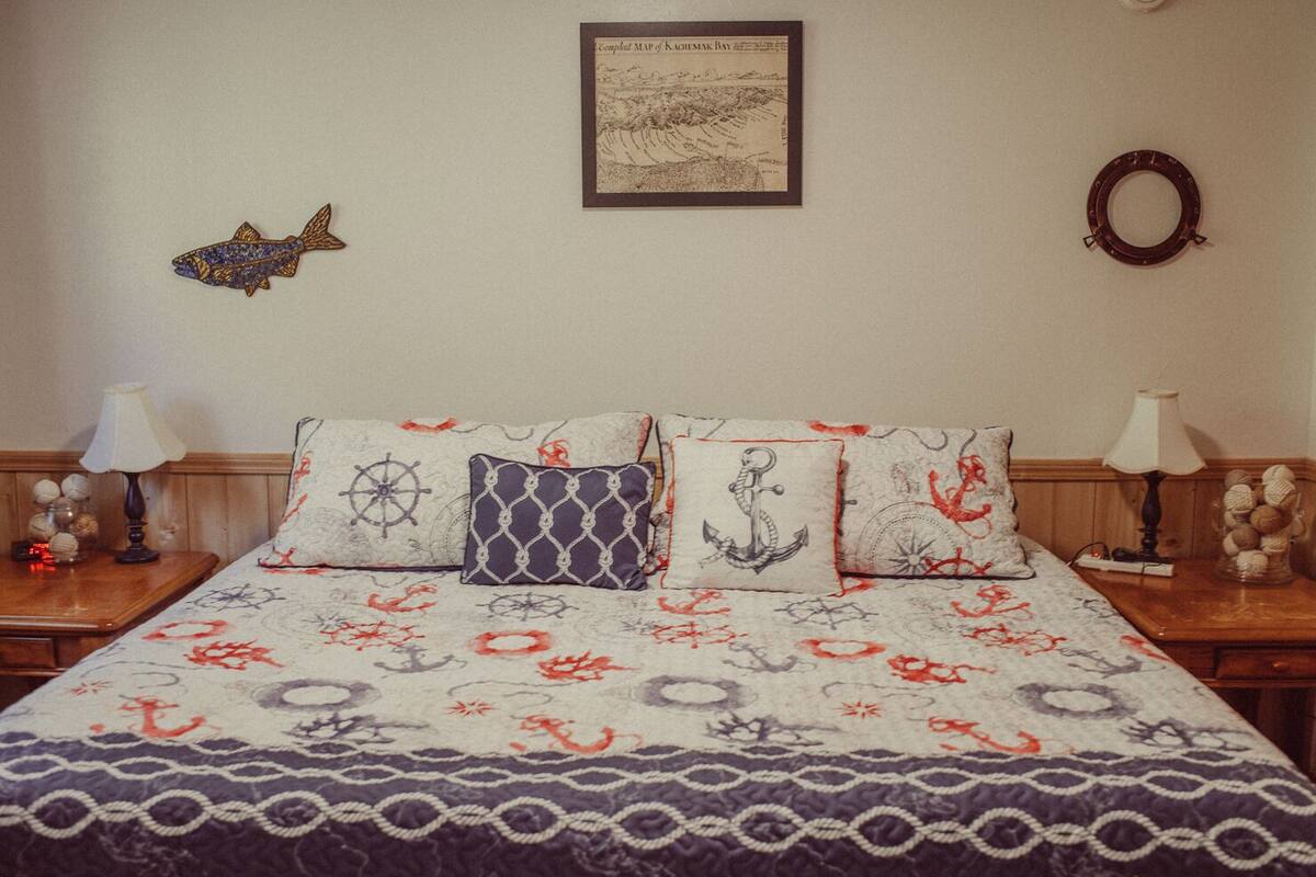 A bedroom with a nautical-themed bedspread, a framed map on the wall, and decorative pillows.