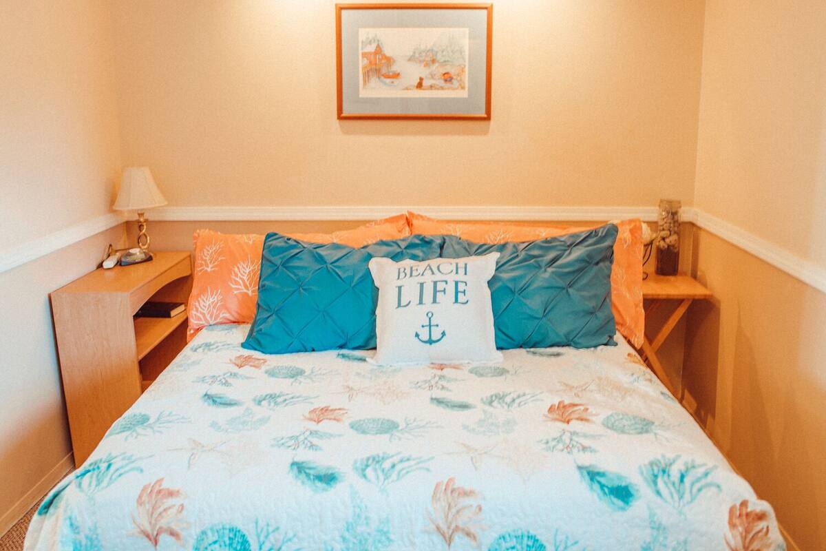 A bedroom with a bed, a nightstand, a lamp, and a framed picture on the wall.