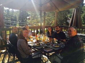 A group of people seated at an outdoor table with food and drinks, under a covered area with string lights. - Meadow Creek Mountain Lodge and Event Center (Pine)