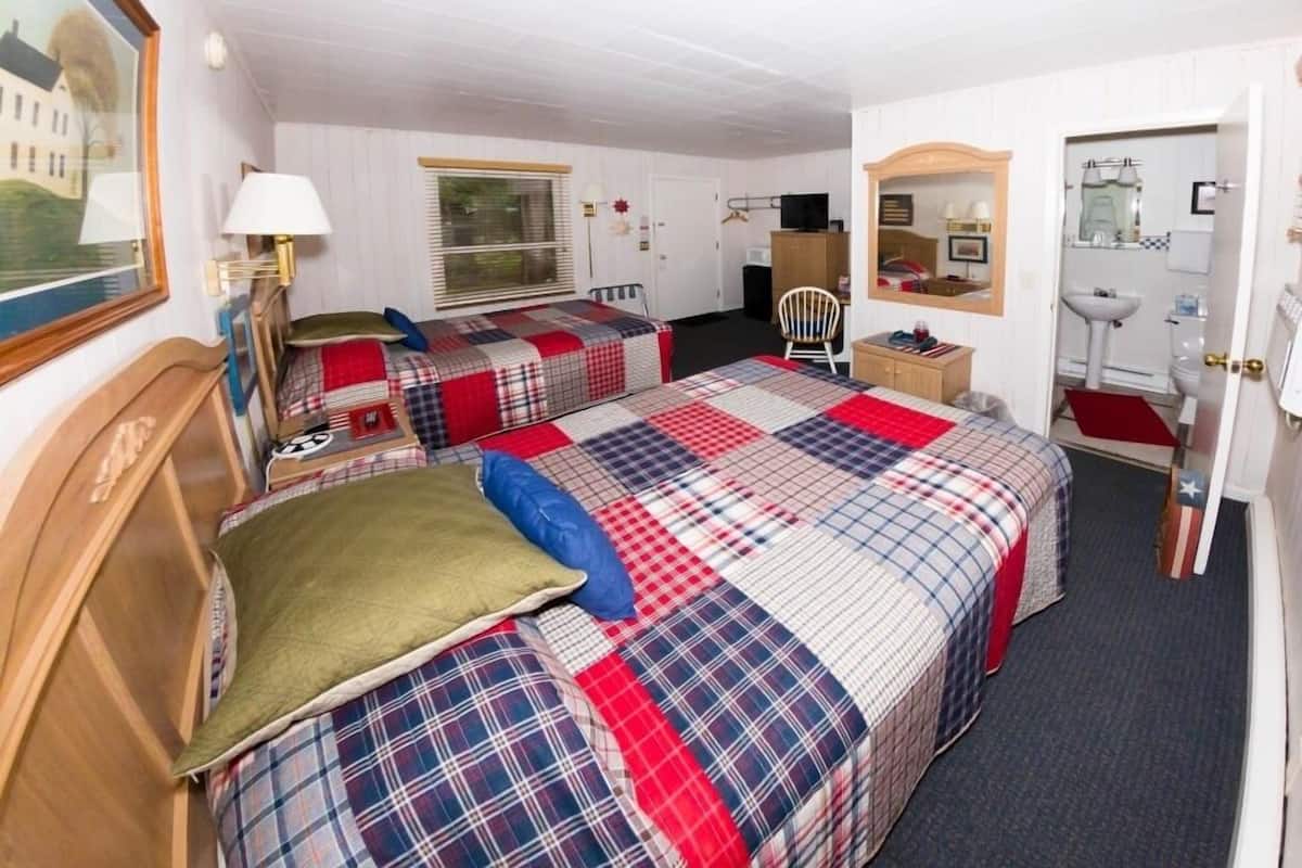 A hotel room with two beds, a desk, a chair, a mirror, and a window.
