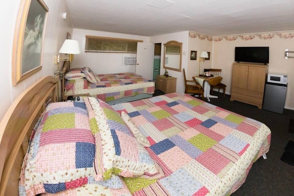 A hotel room with two beds, a desk, a television, and a microwave.