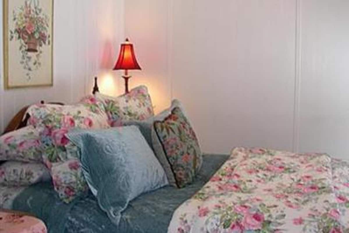 A bedroom with floral bedding, a red lamp, and a framed picture on the wall.
