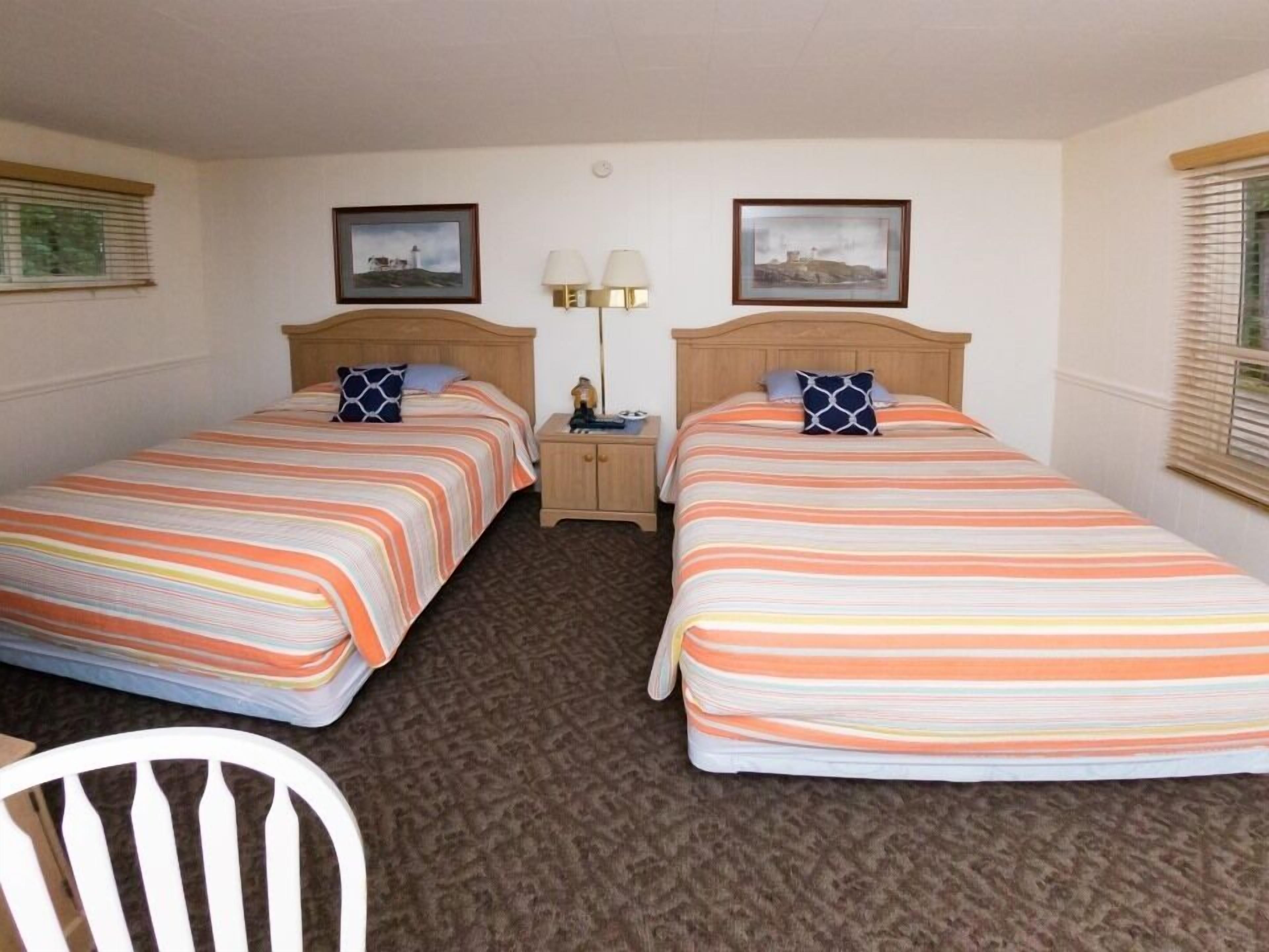 A hotel room with two single beds, a nightstand with lamps, and a chair.