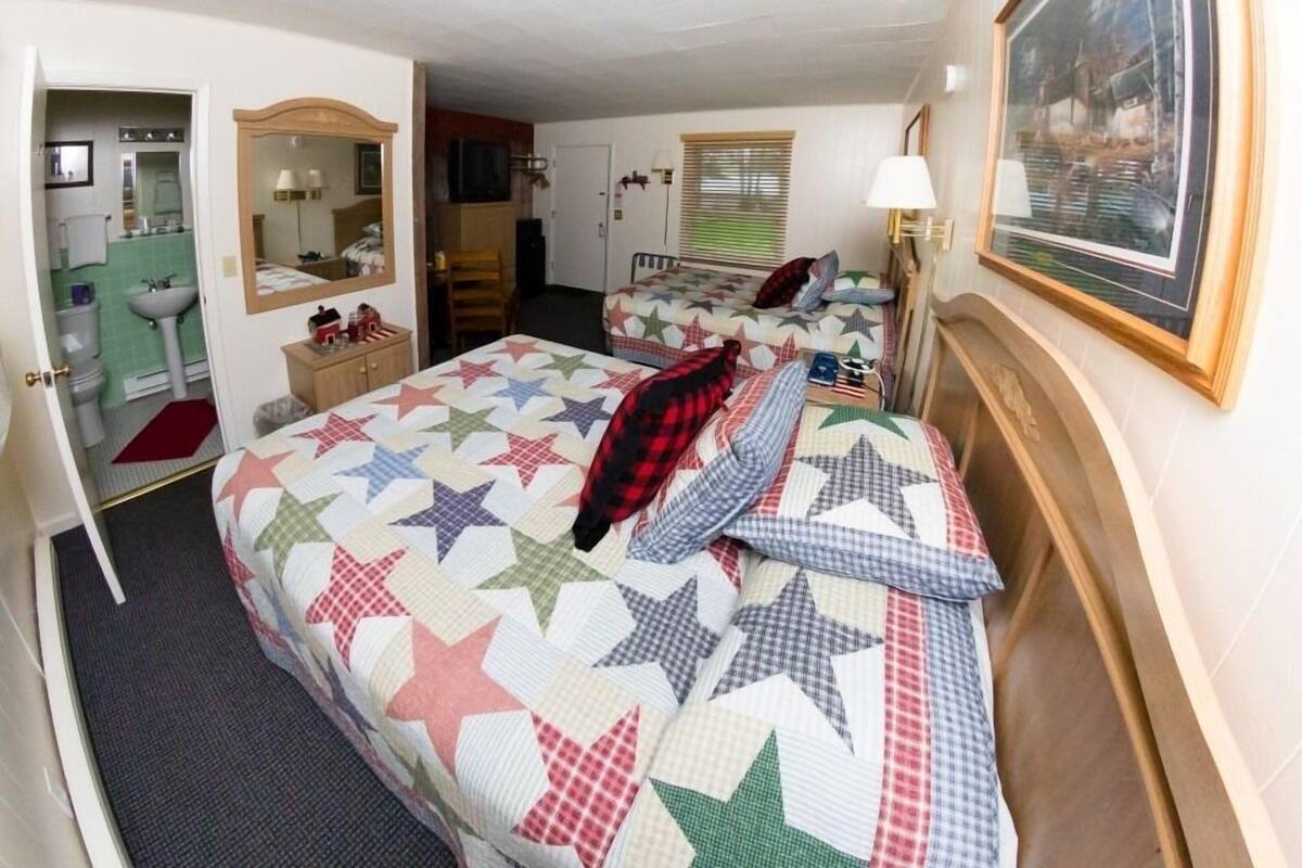 A bedroom with a large bed, a dresser, a mirror, a window with blinds, and a framed picture on the wall.