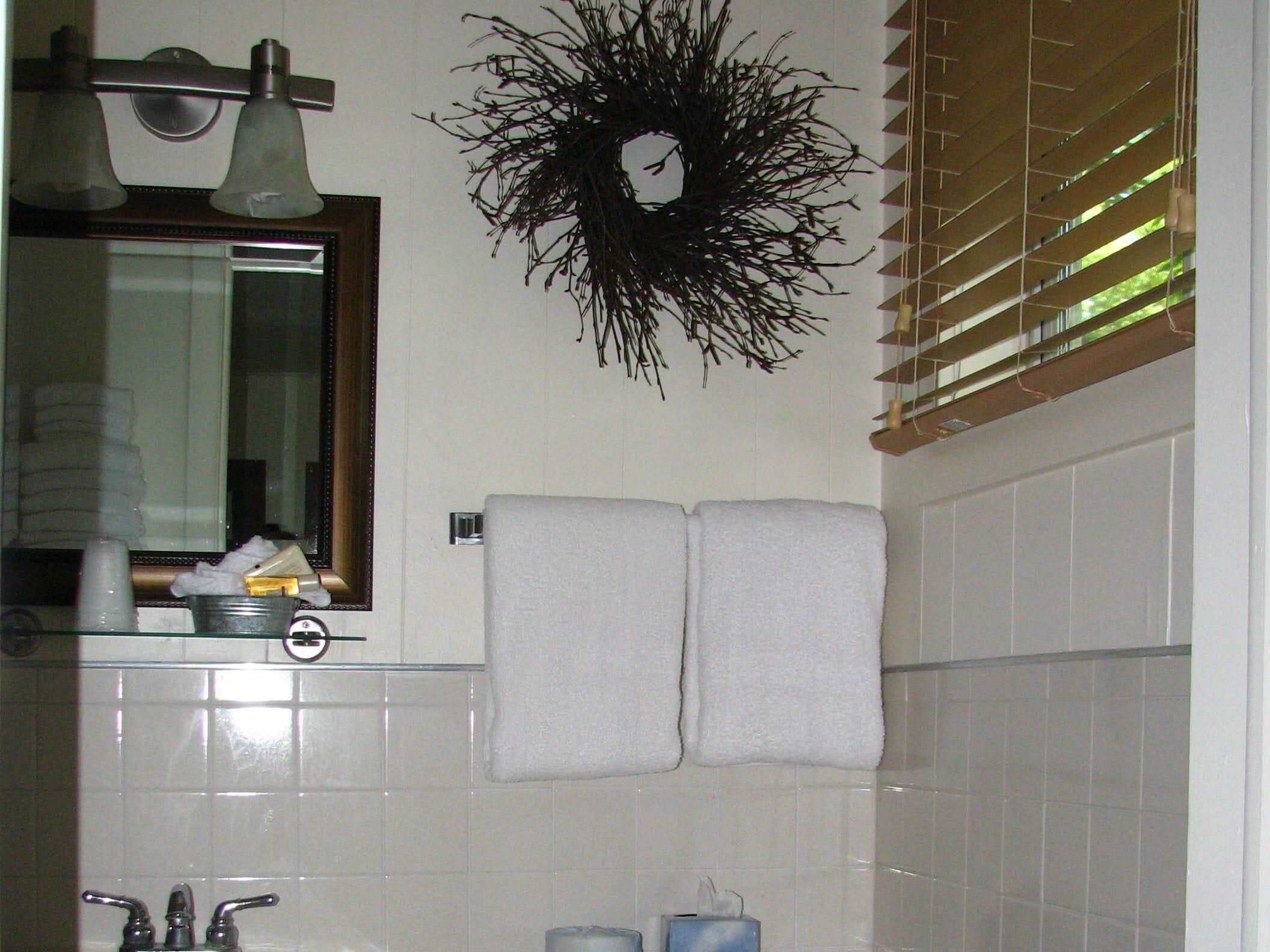 Un baño con lavamanos, espejo, perchero para toallas y una guirnalda decorativa en la pared.