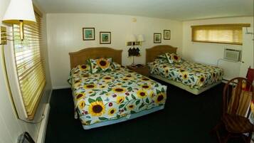 Quarto com duas camas, cada uma com colcha estampada em girassóis, cabeceira de madeira, mesa de cabeceira e uma cadeira.