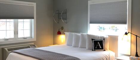 Une chambre bien rangée, avec un grand lit, des tables de chevet, un radiateur et une fenêtre équipée de stores.