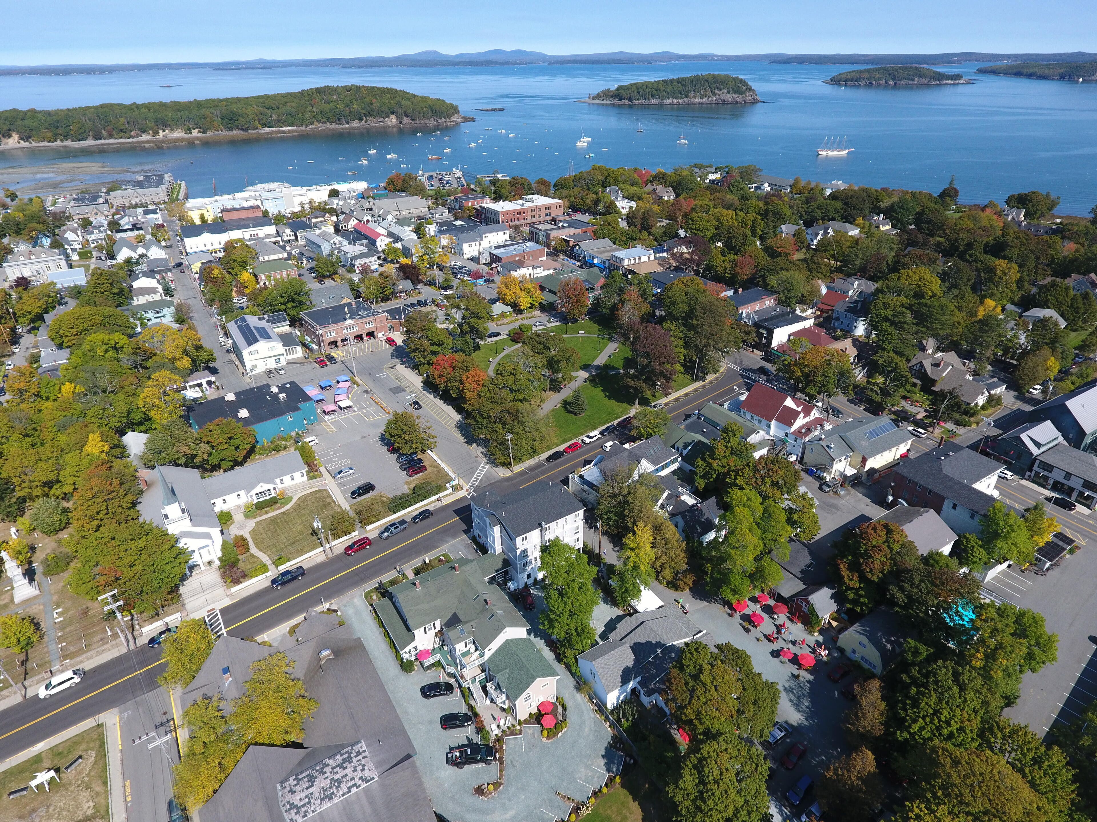 An aerial view of a coastal town with residential buildings, a parking lot, and a marina with boats.