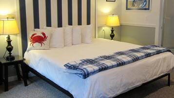 A neatly made bed with a striped headboard, two bedside lamps, a red crab pillow, and a framed picture on the wall.