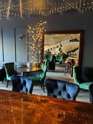 A cozy restaurant interior with green upholstered chairs, a wooden bar counter, and string lights. - Acadia Hotel - Downtown (Bar Harbor)