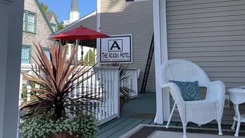 A hotel porch with a white chair, a red umbrella, and a sign for The Acadia Hotel.