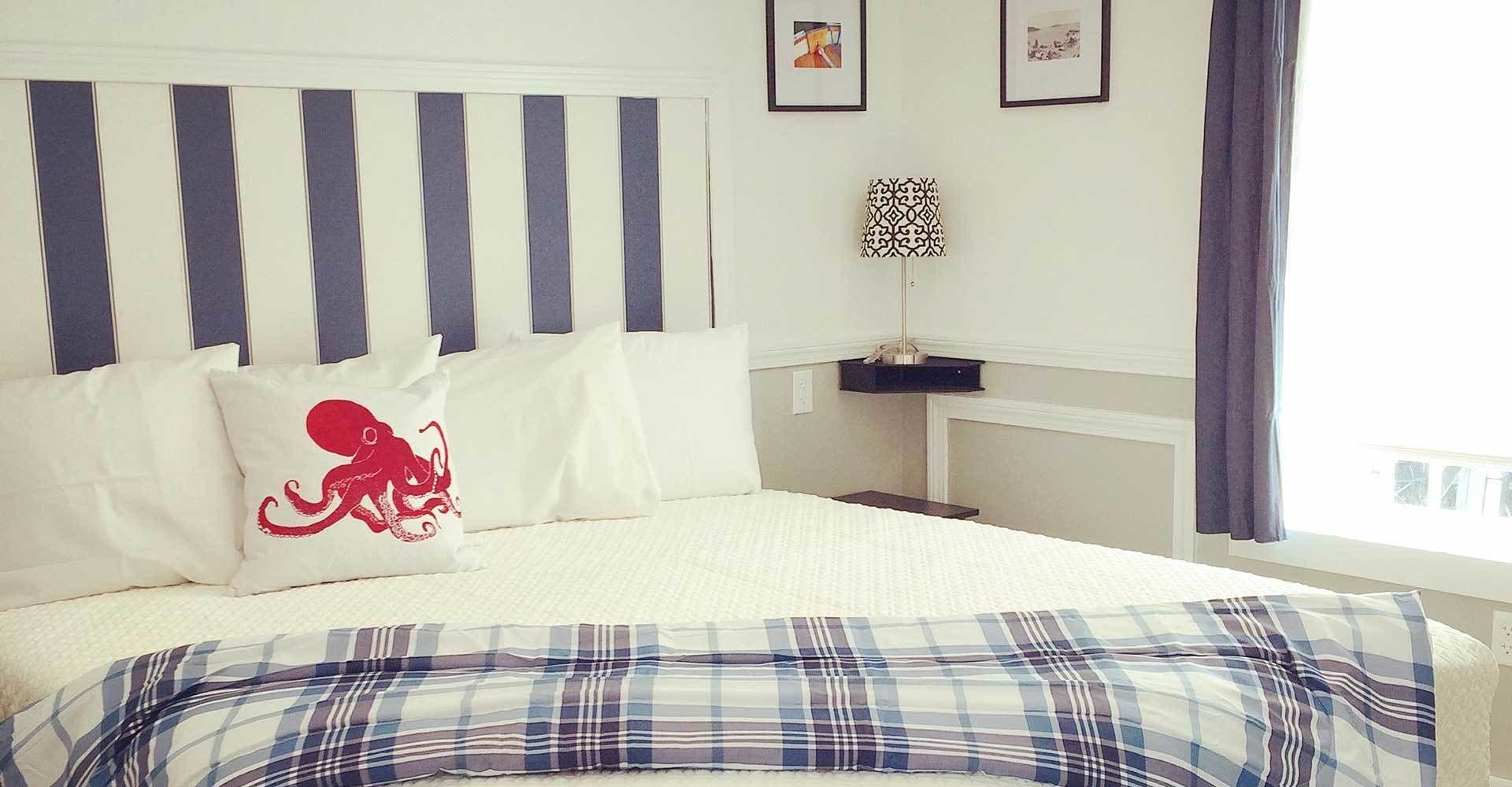 A neatly made bed with striped headboard, a plaid bedspread, and a pillow with an octopus design.