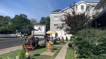 Un área de estar al aire libre con mesas y sillas, un cartel de The Acadia Hotel y una cerca de piquetes blancos.