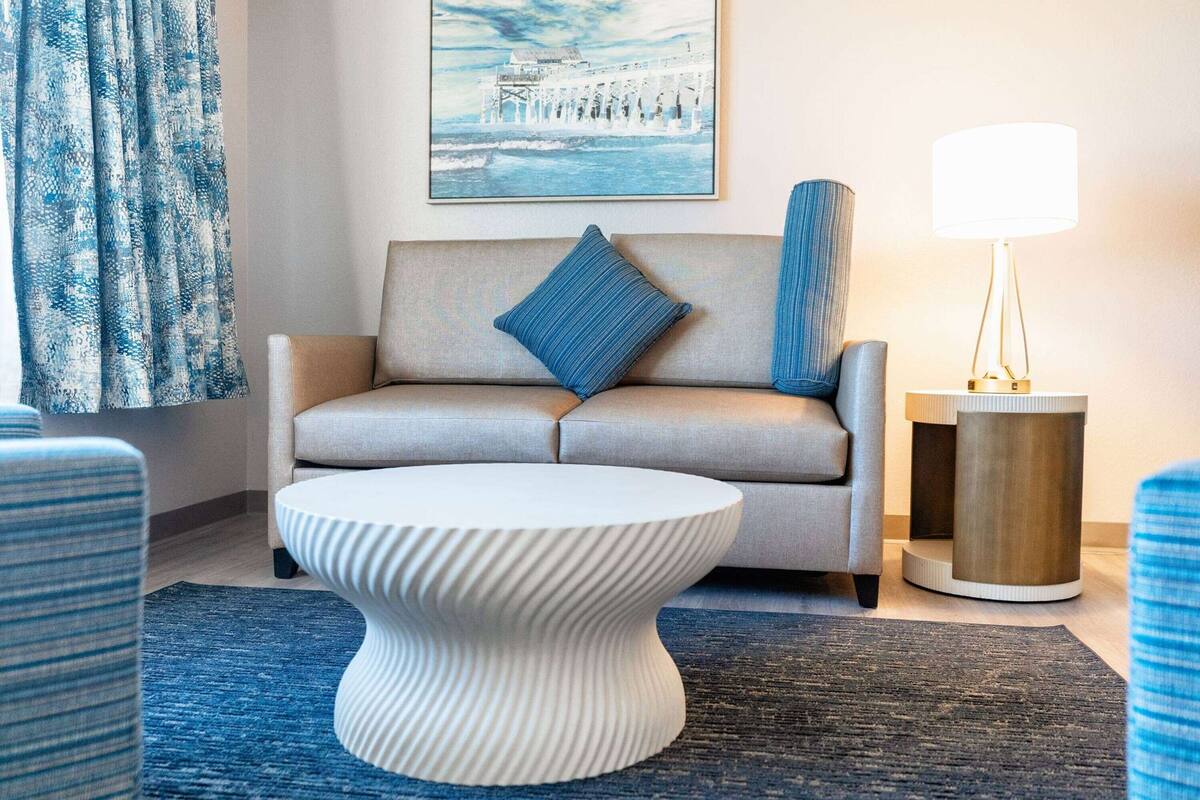 A modern living room with a sofa, a round coffee table, a lamp, and a framed picture on the wall.
