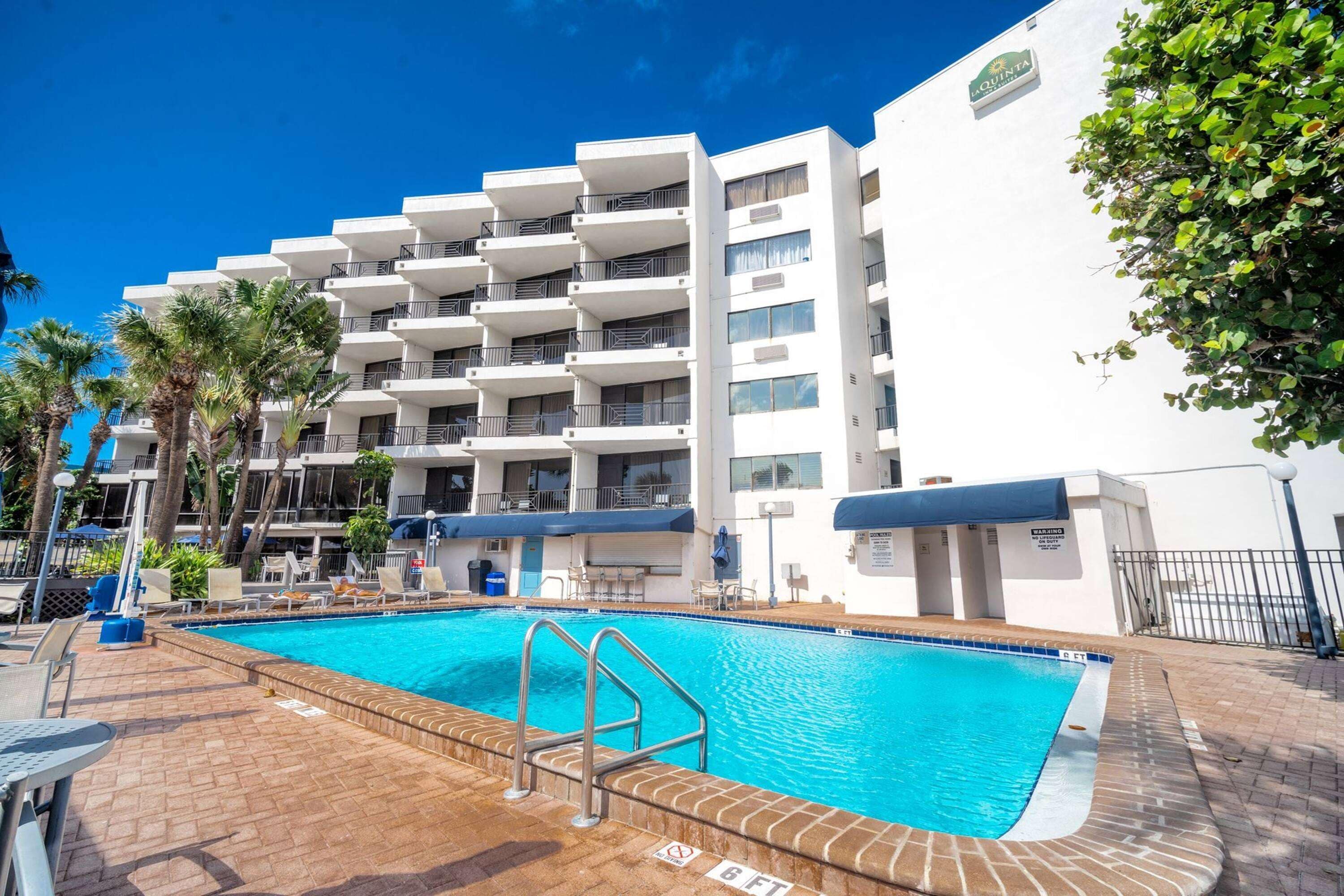 Un hôtel doté d’une piscine, de palmiers et d’une façade blanche.