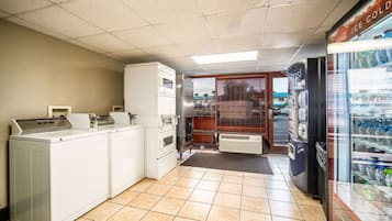 A laundromat with multiple washers and dryers, a vending machine, and a Coca-Cola refrigerator.