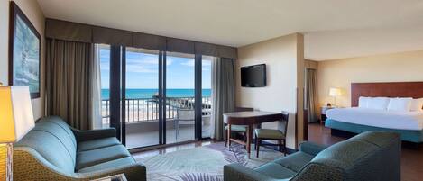 A hotel room with a balcony, a bed, a desk, and two sofas.