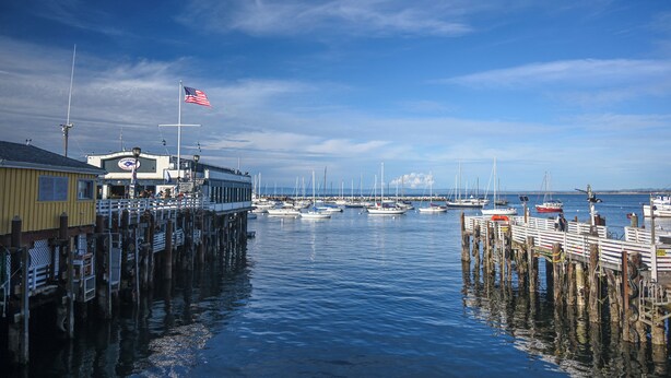 A marina with boats docked, a pier with a flag, and a building with a sign.