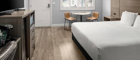 A hotel room with a bed, a desk, a TV, and a window with blinds.