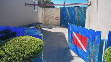 Une entrée fermée par un portail, avec un mur en pierre et un portail bleu orné d’une bande rouge en diagonale.