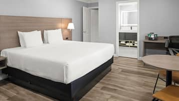 Una habitación de hotel con una cama grande, mesita de noche, lámpara y una pequeña mesa redonda con sillas.