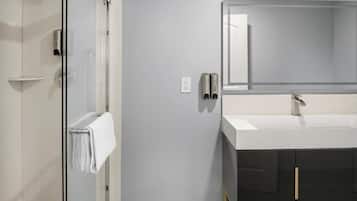 A modern bathroom with a glass shower enclosure, a white sink with a large mirror, and black cabinets.