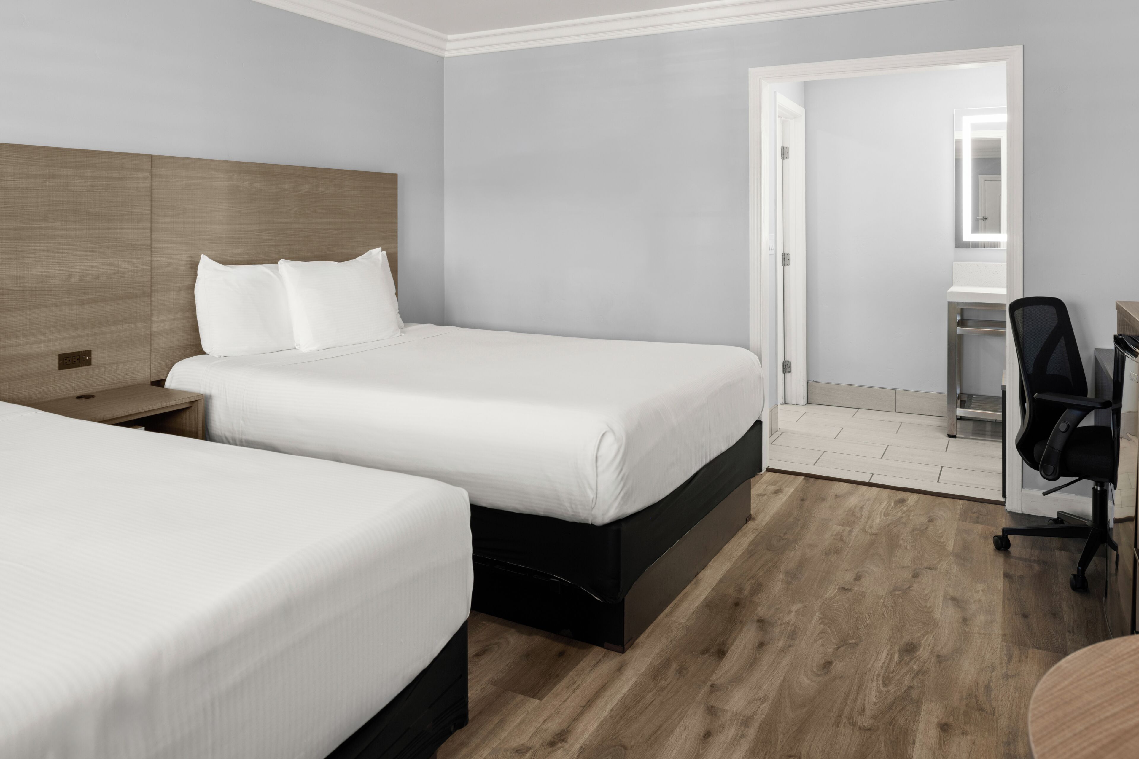 Una habitación de hotel con dos camas, un escritorio con una silla y un espejo.