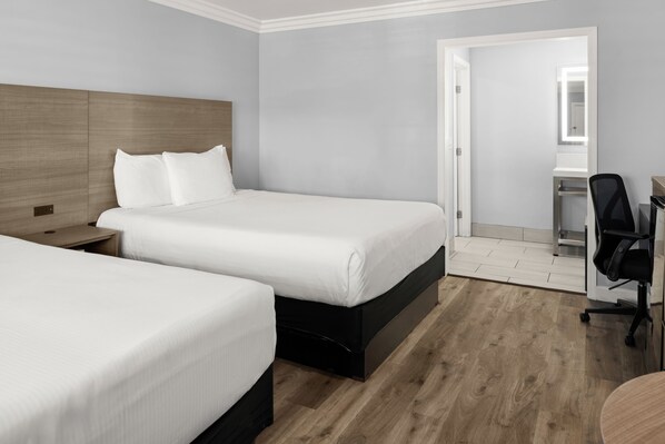 A hotel room with two beds, a desk with a chair, and a mirror.