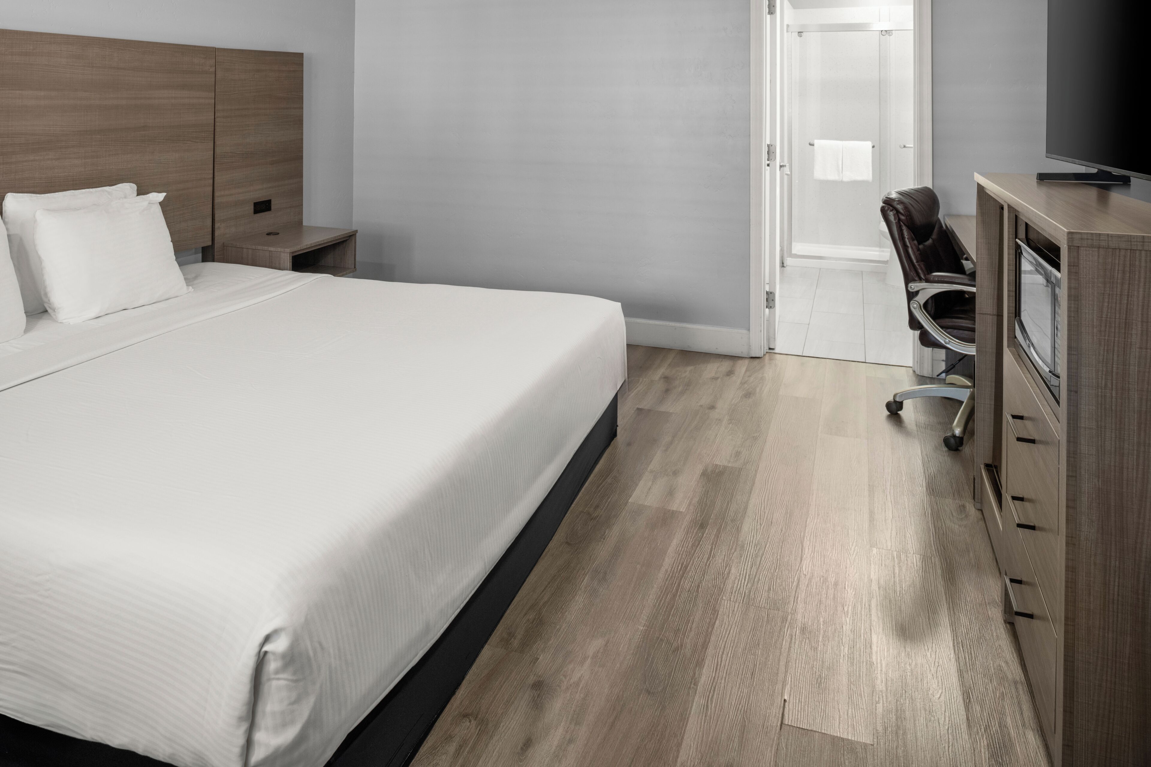 A hotel room with a bed, a desk, a chair, a television, and a shower area.