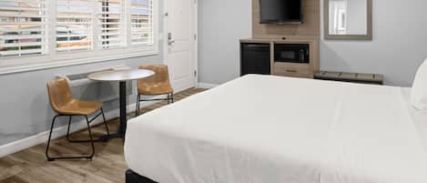Habitación de hotel con cama, televisión, escritorio y silla, y ventana con persianas.