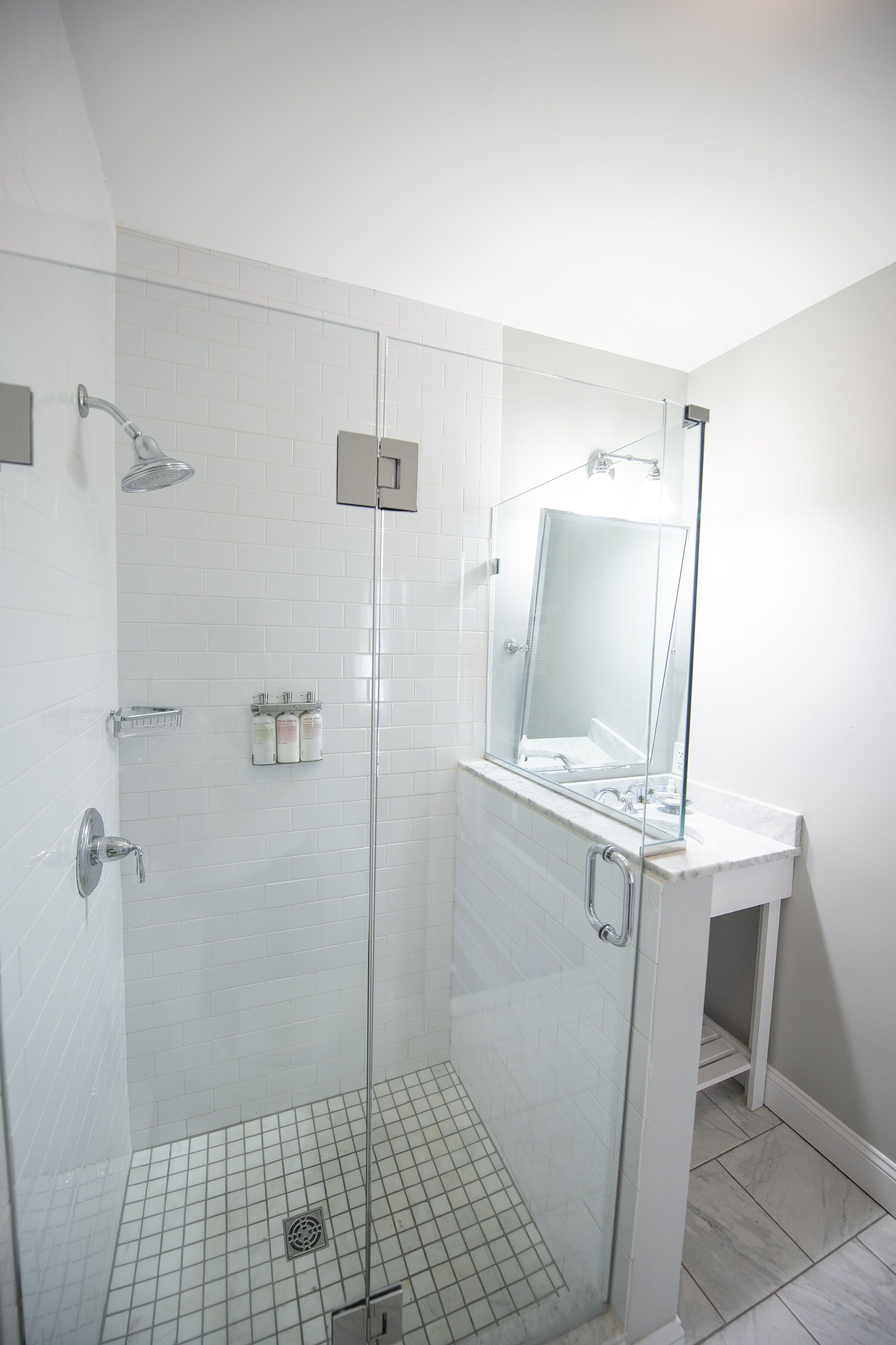 A modern bathroom with a glass-enclosed shower, a white tiled wall, and a large mirror above the sink.