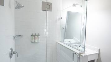A modern bathroom with a glass-enclosed shower, a white tiled wall, and a large mirror above the sink.