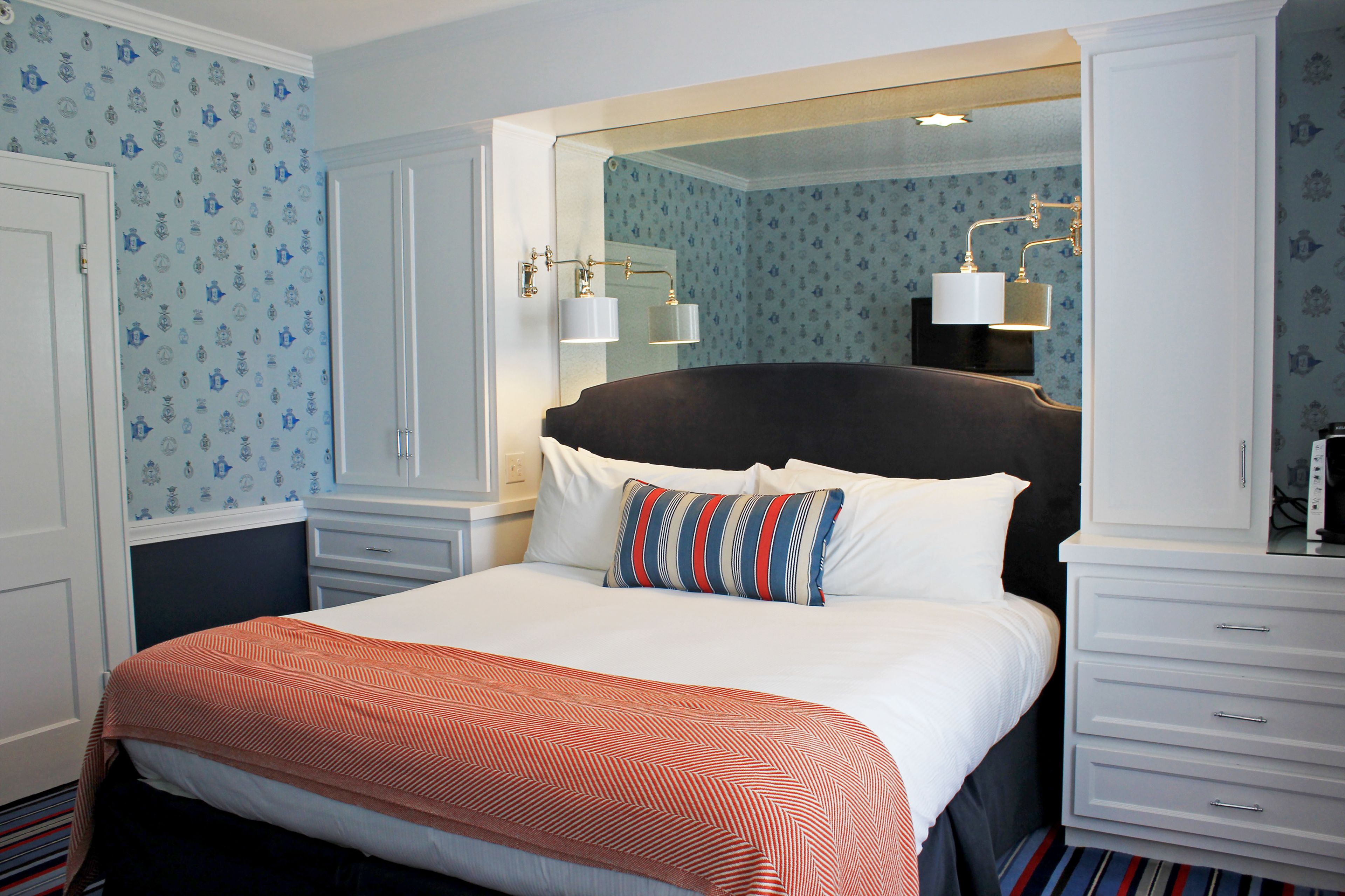 A neatly arranged hotel room with a large bed, a dresser, and a mirror above the bed.