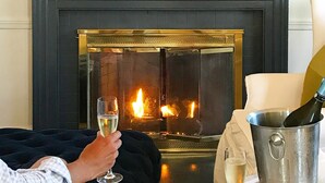 A cozy room with a fireplace, a bookshelf, a table with a bottle of champagne, and a glass of wine. - Kennebunkport Inn (Kennebunkport)