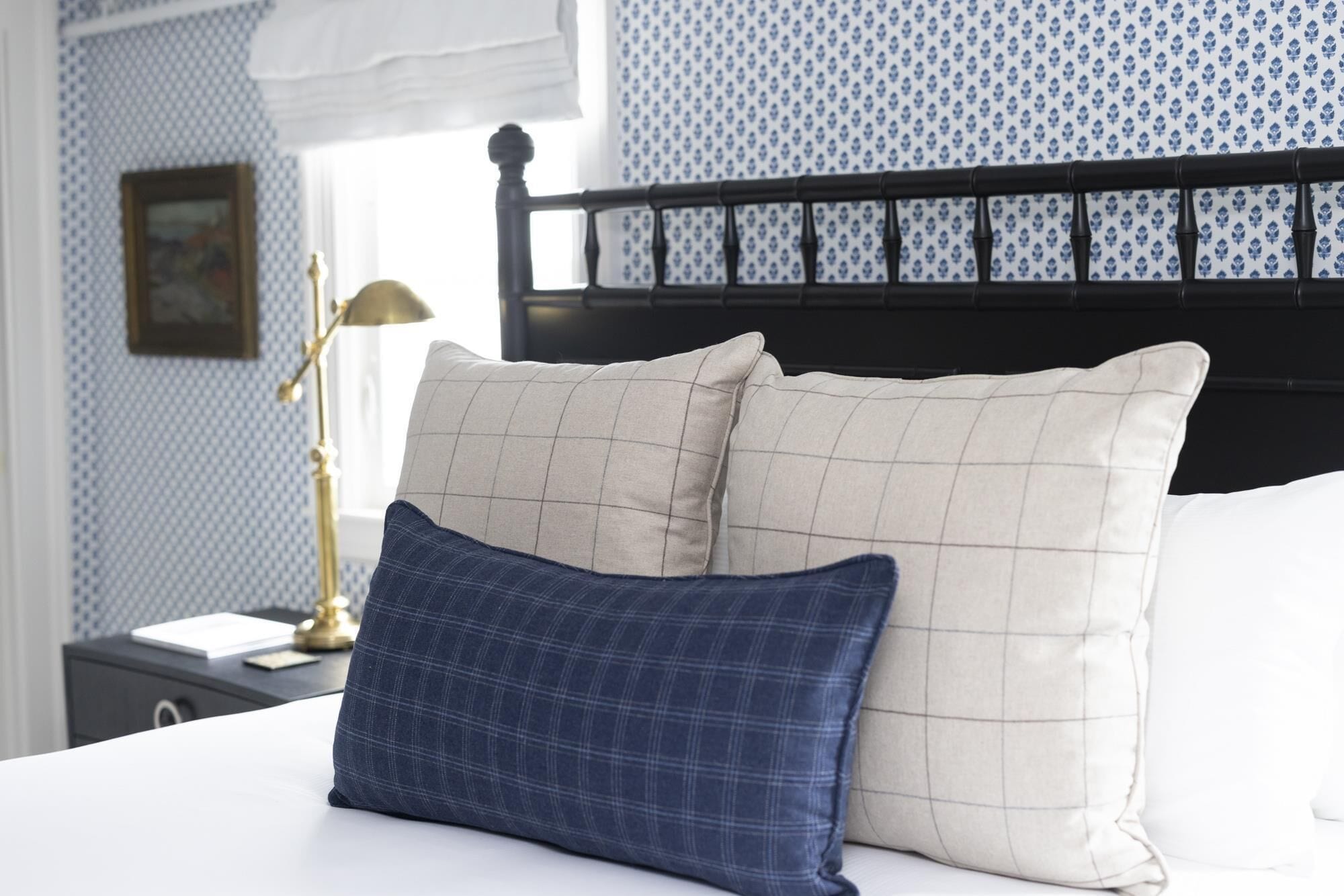 Un lit avec deux oreillers, un bleu et un beige, dans une chambre dont le papier peint est à motifs et qui possède une tête de lit noire.