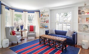 A cozy living room with a blue sofa, striped chairs, a coffee table, and a bookshelf filled with books and decorative items.