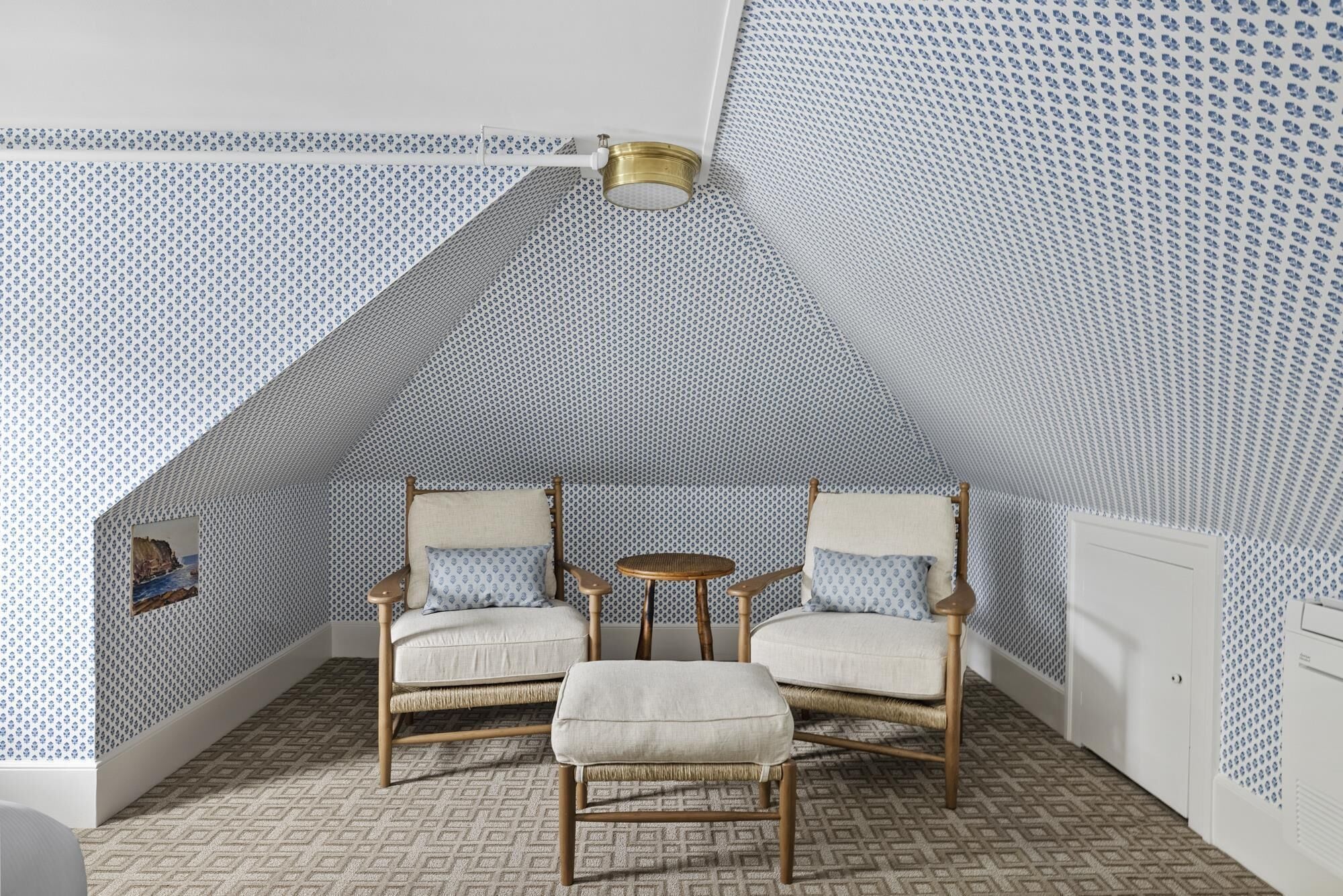 A cozy attic room with patterned wallpaper, two wicker chairs, a small round table, and a ceiling light fixture.