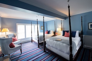 A four-poster bed with white bedding and red and blue pillows, a striped carpet, and a blue wall.