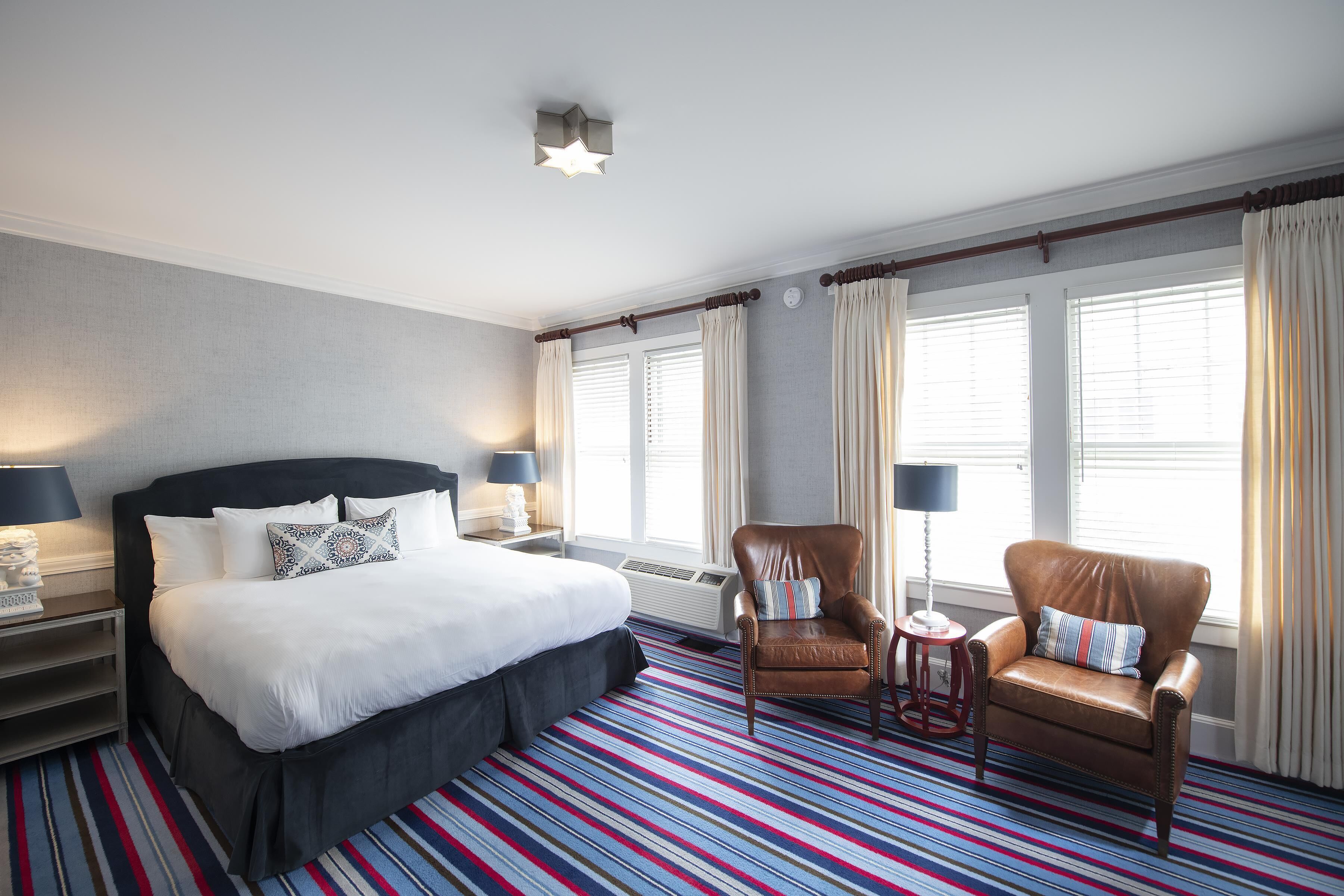 A hotel room with a large bed, two armchairs, a small table, and a window with curtains.