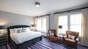 A hotel room with a large bed, two armchairs, a small table, and a window with curtains.
