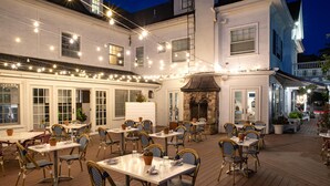 An outdoor dining area with tables and chairs, string lights, and a stone fireplace. - Kennebunkport Inn (Kennebunkport)