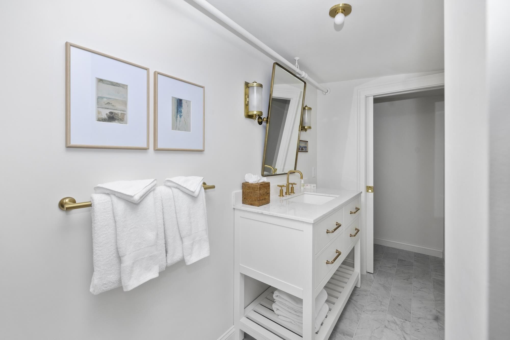 Een badkamer met een witte wastafel, gouden details en twee ingelijste foto's aan de muur.