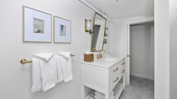 Une salle de bain avec un meuble-lavabo blanc, des robinetteries dorées et deux tableaux encadrés au mur.