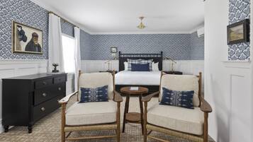 A hotel room with a bed, two armchairs, a small table, a dresser, and patterned wallpaper.