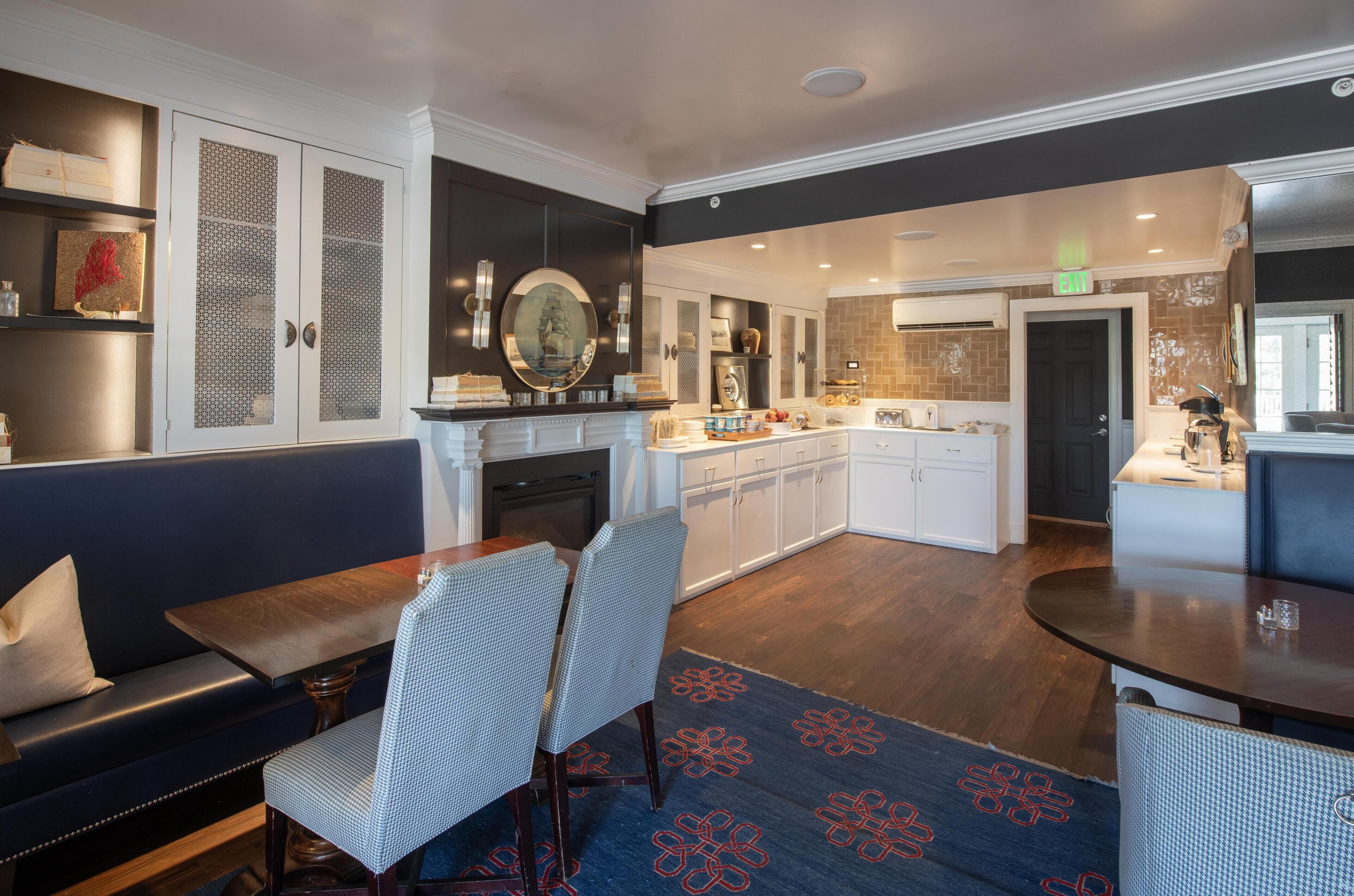 A modern kitchen with white cabinets, a central island, and a dining area with a blue patterned rug.