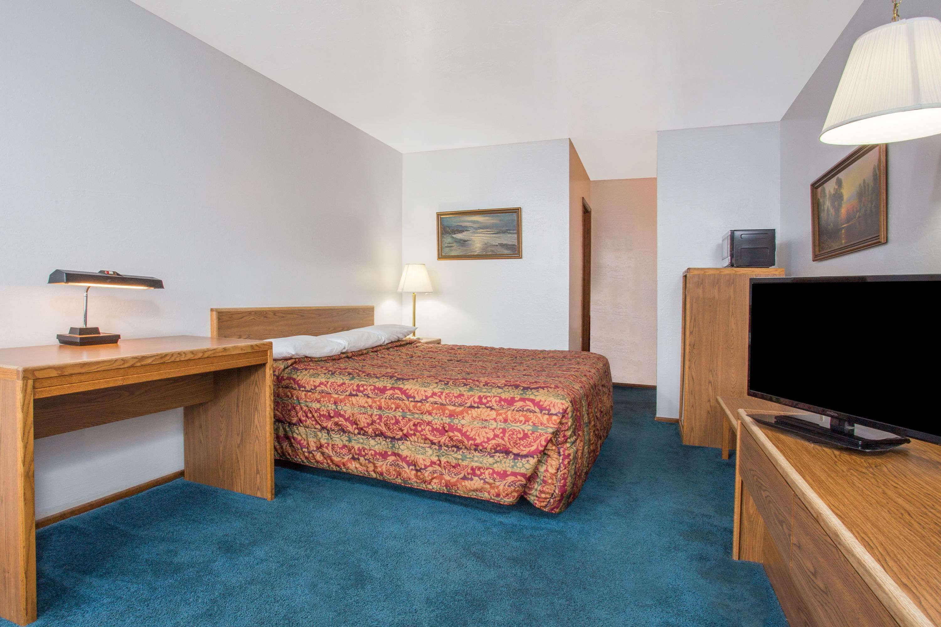 A hotel room with a bed, a desk, a television, and a lamp.