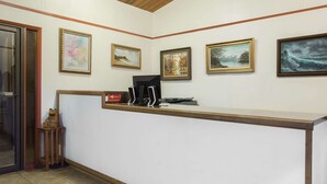 A reception desk with framed artwork on the wall, a small wooden stool, and a sign. - Knights Inn Boardman (Boardman)