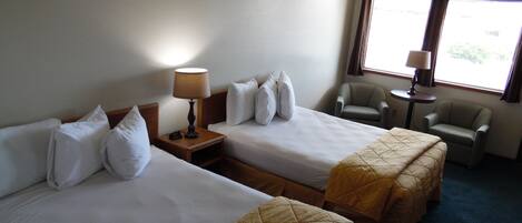 A hotel room with two beds, a chair, a small table, and a window with curtains.